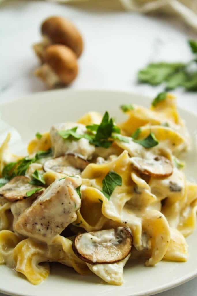 instant Pot Chicken Stroganoff on a white plate with fresh mushrooms in the background