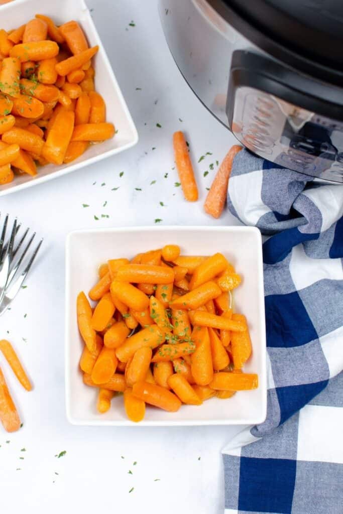 Glazed carrots in a white square bowl with white and blue checkered tablecloth and Instant Pot next to it