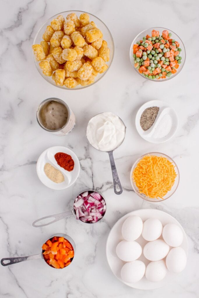 Ingredients needed to make tater tot casserole without meat: eggs, sour cream, cream of mushroom soup, frozen peas and carrots, onion, red bell pepper, seasonings, frozen tater tots, and cheese.