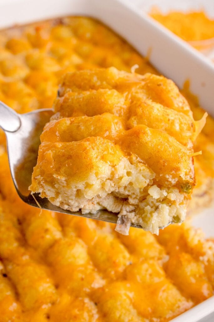 Slice of the tater tot casserole with no meat being picked up with a serving spatula above the casserole dish of it.