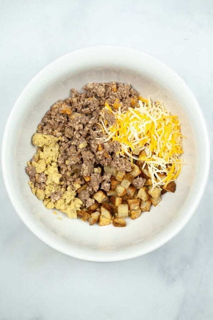 Potatoes, ground sausage, scrambled eggs, and cheese mixed together in a bowl