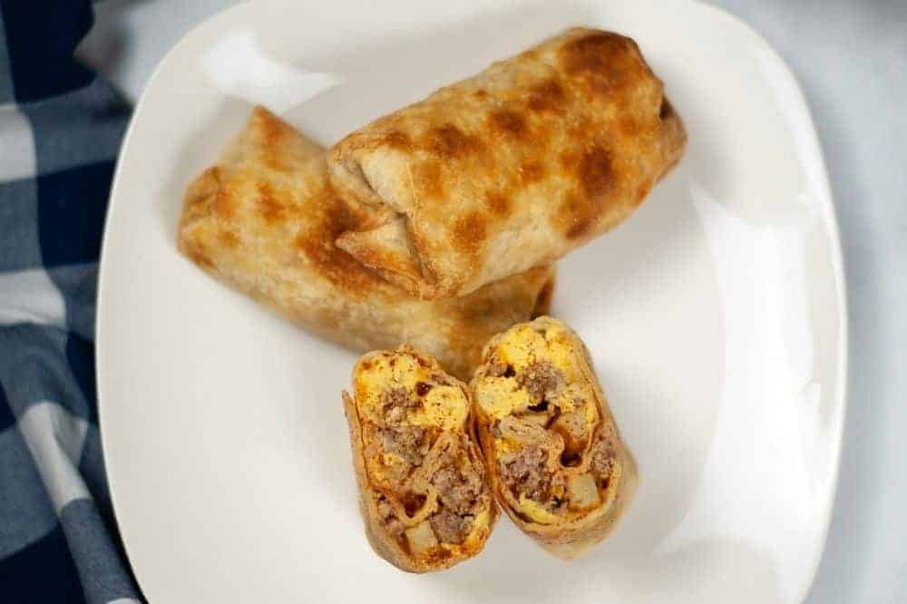 Overhead photo of the breakfast chimichangas. Two full cooked burritos stacked on plate and one burrito cut in half place right side up so you can see the inside
