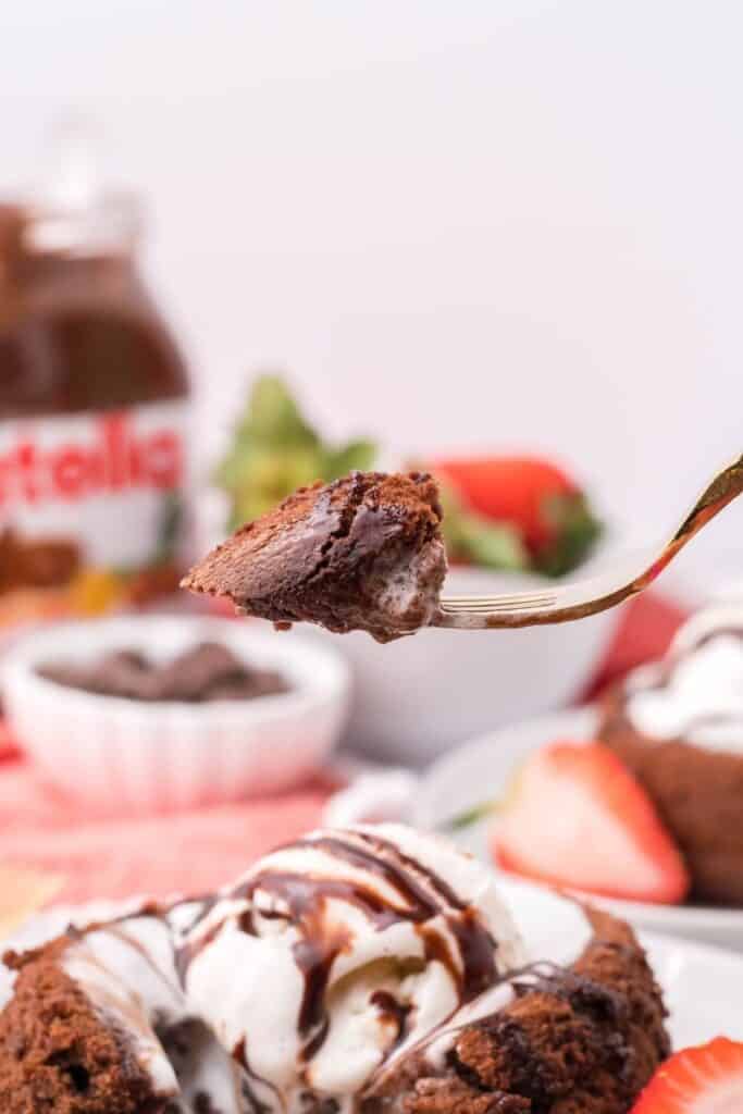 Bite of Nutella Lava Cake on a fork with Nutella container in back and chocolate lava cake in forefront