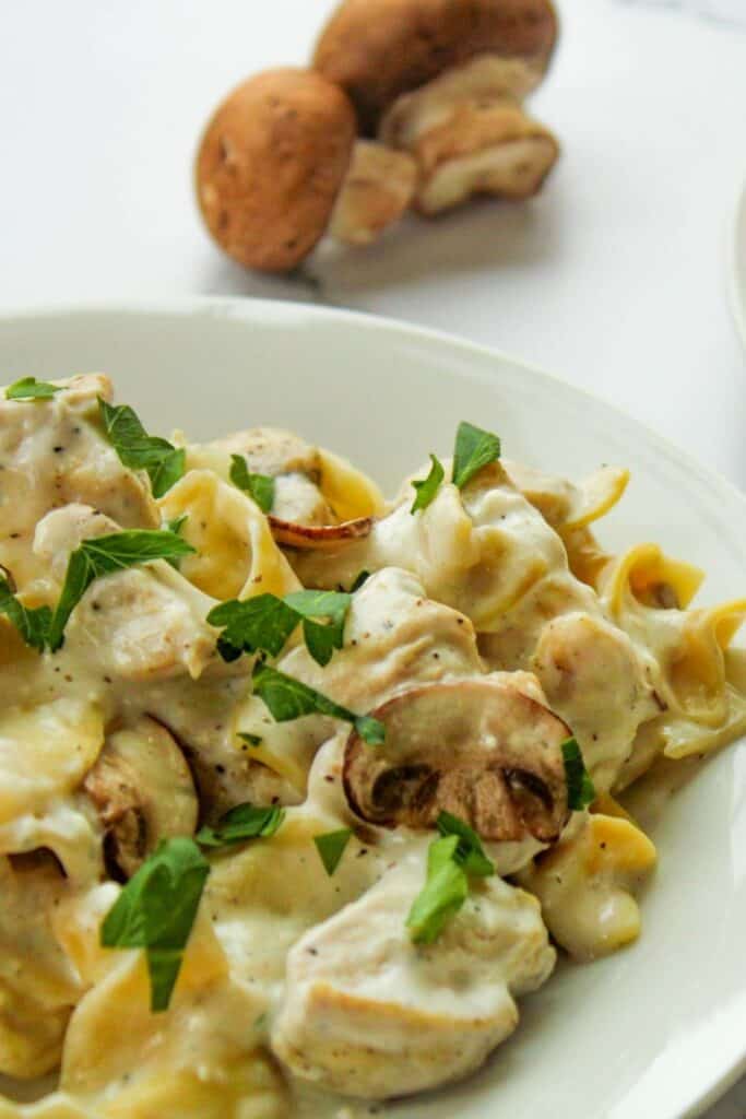 Instant Pot Chicken Stroganoff with parsley on a white plate with fresh mushrooms in the back