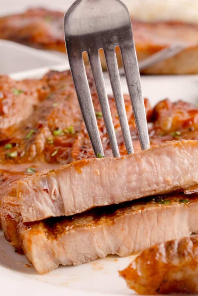 Close up of the air fry pork steak slices stacked on top of each other using a fork to see the inside cooked and moist.