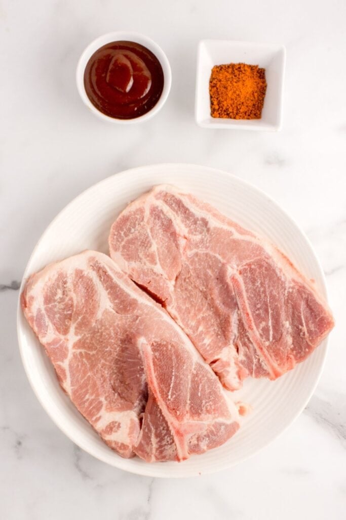 Ingredients needed to make a pork steak in the air fryer: pork butt steaks, BBQ dry rub, and BBQ sauce.