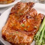 Pork steaks in the air fryer on a white plate served with asparagus.