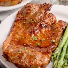 Pork steaks in the air fryer on a white plate served with asparagus.