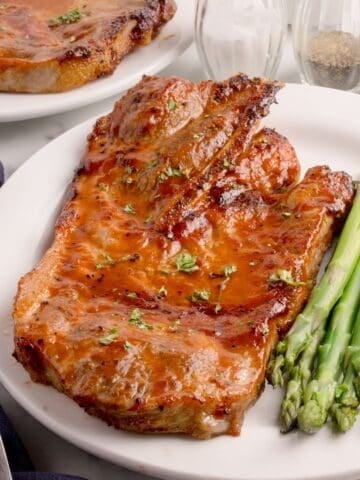 Pork steaks in the air fryer on a white plate served with asparagus.