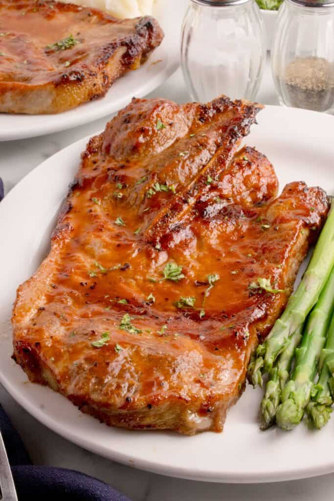 Pork steaks in the air fryer on a white plate served with asparagus.