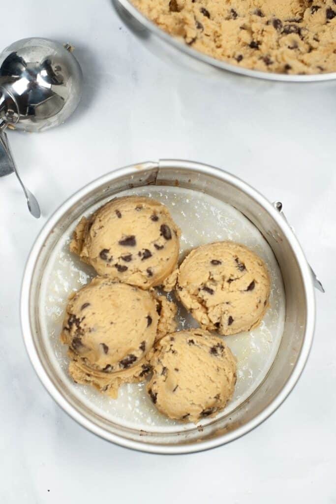 Scoops of raw cookie dough inside a spring form pan before being pressed down