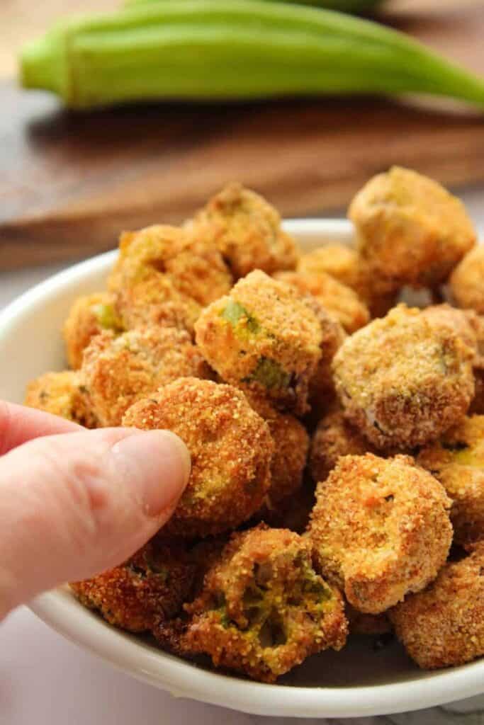 Air Fryer Okra in a bowl with hand picking a piece out