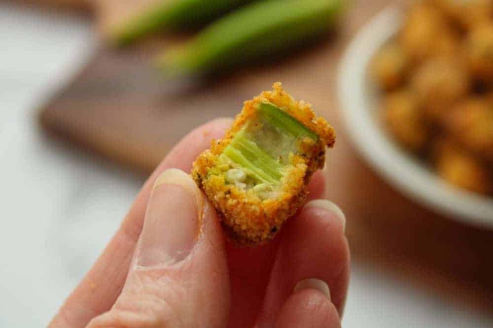 Holding a piece of air fryer okra bitten into in a hand