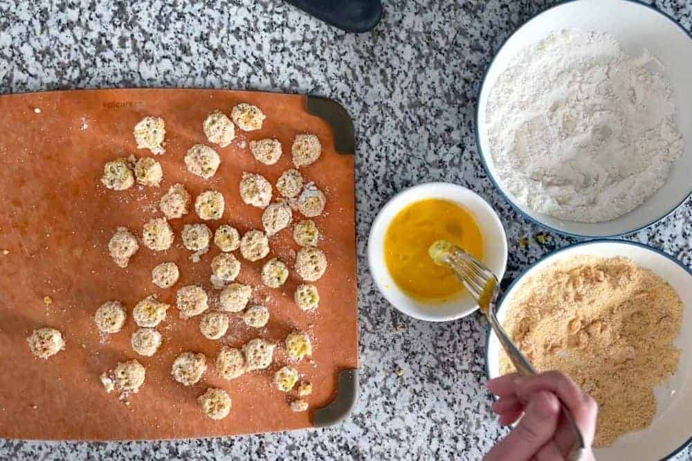 Breading okra pieces on a cutting board and dipping one piece into the egg with a fork