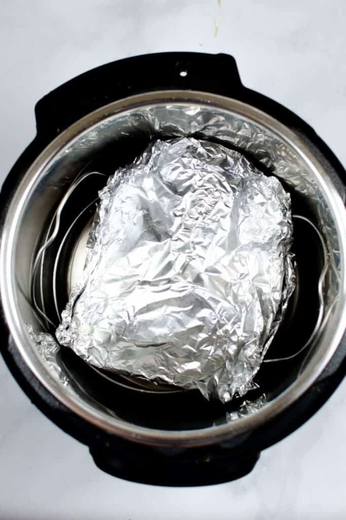Tilapia wrapped in foil on top of a trivet and water inside the Instant Pot