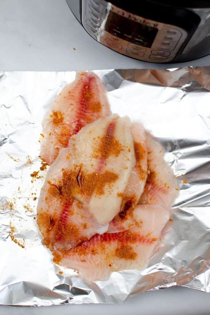 Frozen tilapia with seasoning on top of a piece of aluminum foil