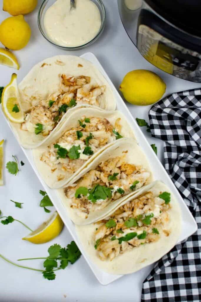 Instant Pot Tilapia Tacos put together in soft shells on a white rectangular serving plate with cilantro sprinkled on top