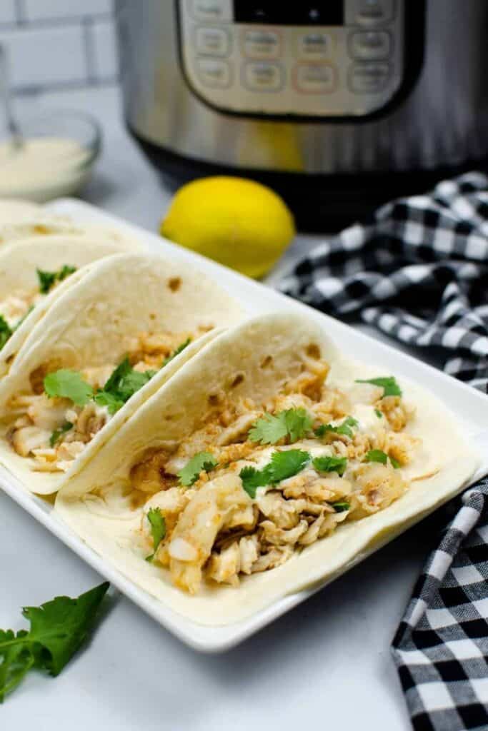 Pressure Cooker Frozen Tilapia served in soft-shelled taco shells on a rectangular white serving dish