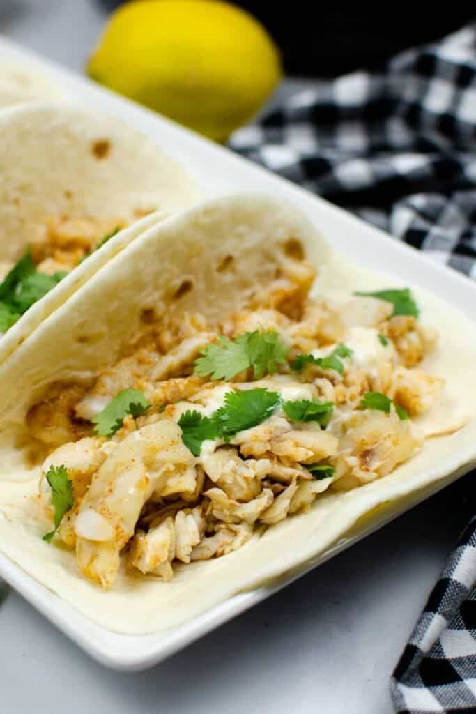 Closeup of Instant Pot Fish Tacos on a white rectangular serving plate with a lemon i nthe background