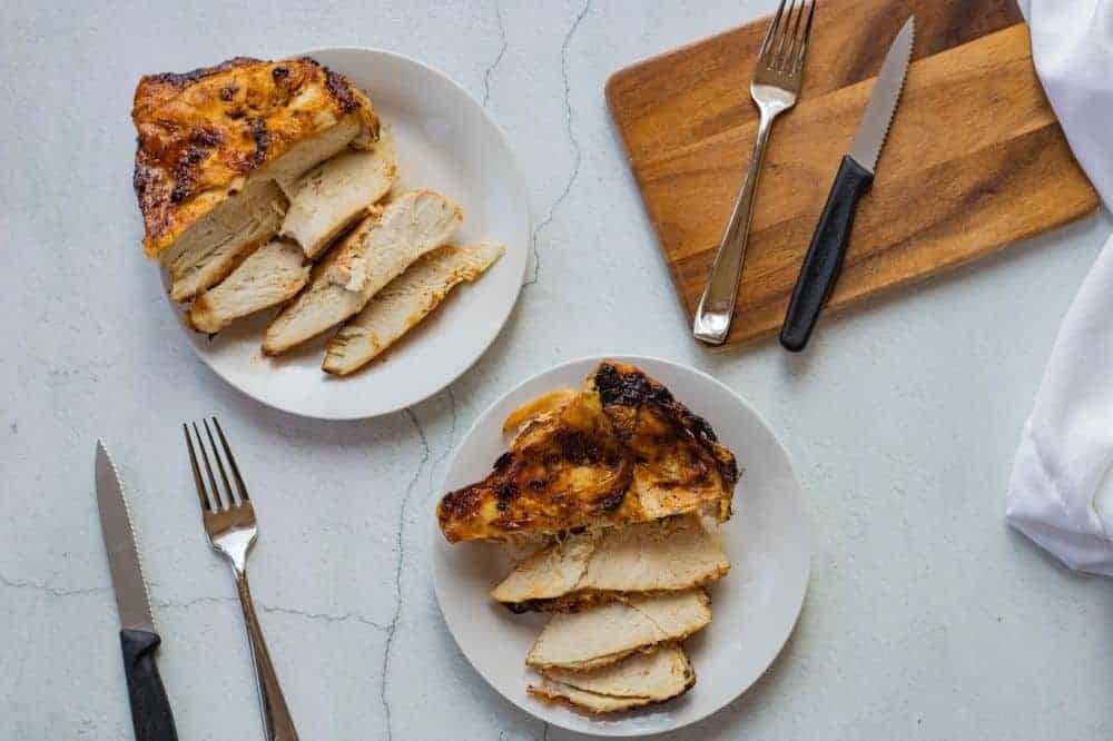 Overhead photo of two chicken breasts on white plates with a knife and fork for each