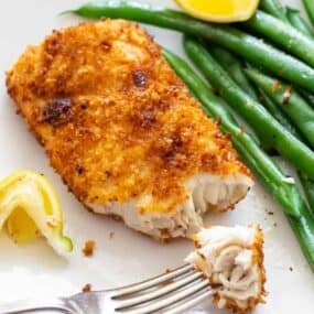 Air Fryer Mahi Mahi with a bite on a fork served with green beans and a slice of lemon
