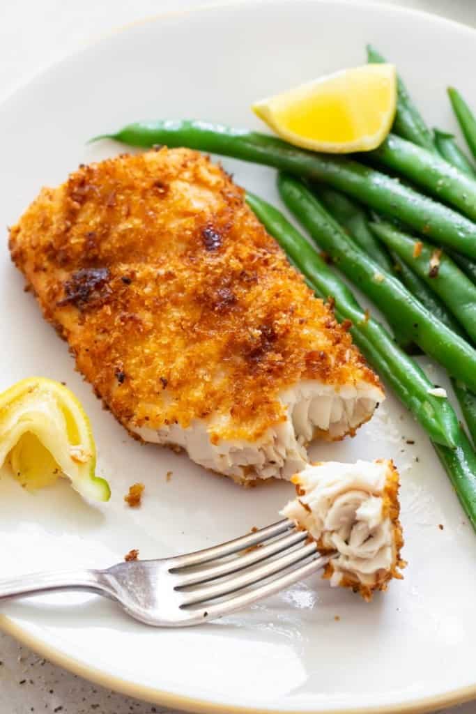 Air Fryer Mahi Mahi with a bite on a fork served with green beans and a slice of lemon