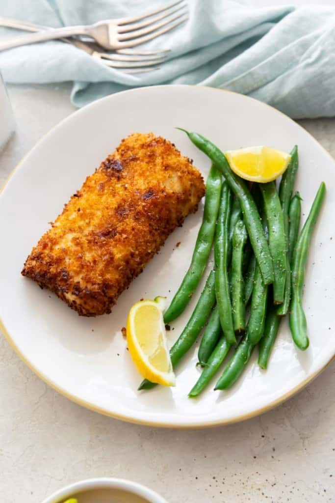 Panko breaded mahi mahi on plate with green beans and lemon wedges