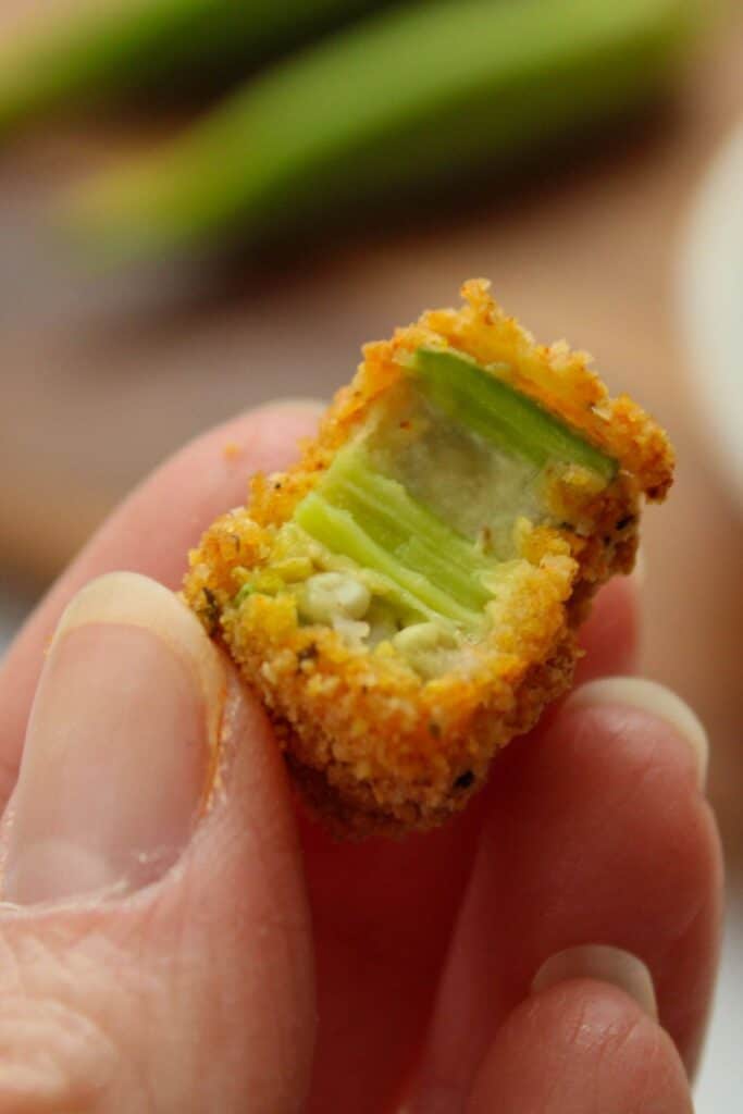 Close up of a hand holding air fryer okra with a bite taken out of it.