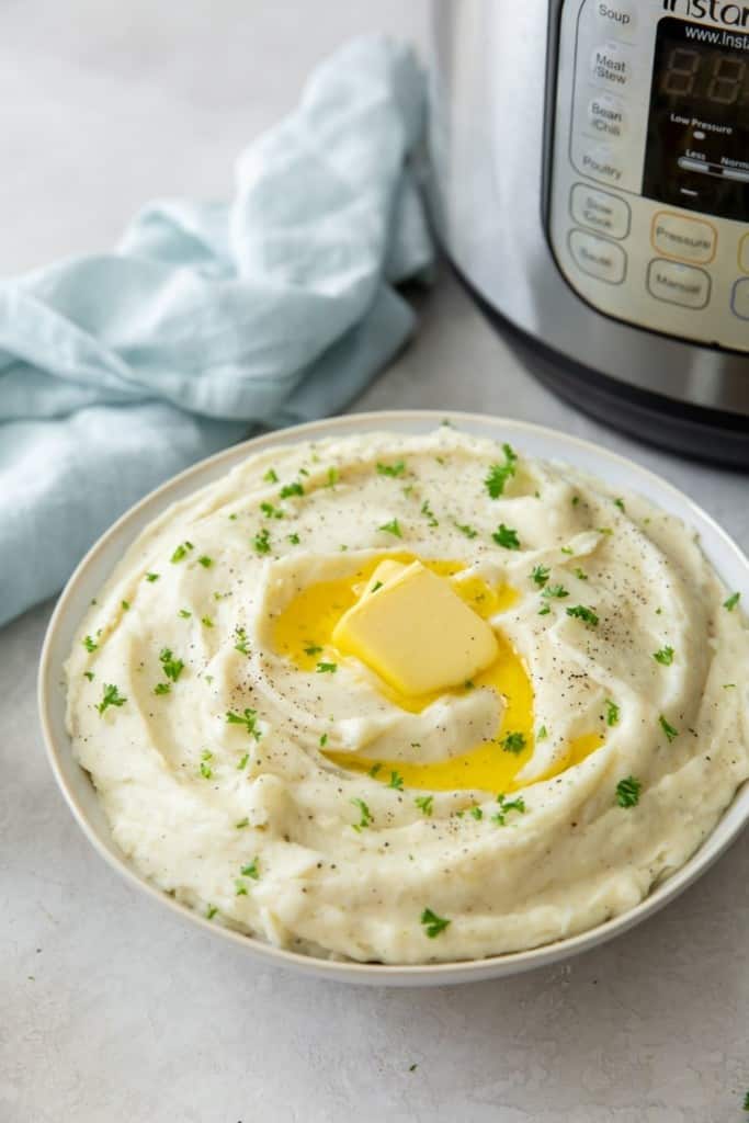 Pressure cooker garlic mashed potatoes in a bowl with butter melting in front of an Instant Pot