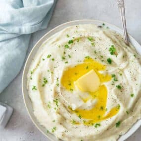Instant Pot Garlic Mashed Potatoes with sour cream in a white bowl with butter melting on top and a spoon inside the bowl