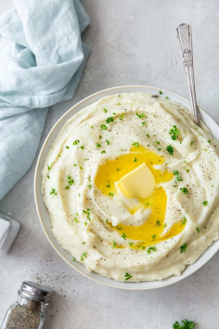 Instant Pot Garlic Mashed Potatoes with sour cream in a white bowl with butter melting on top and a spoon inside the bowl