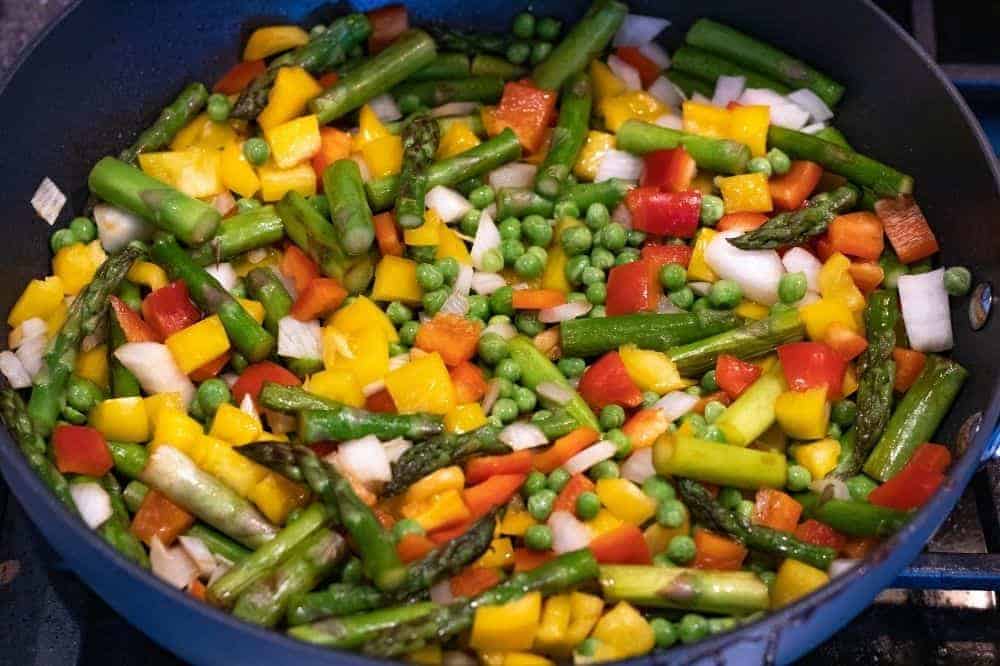 Asparagus, diced sweet peppers, onions, and peas being cooked in a pan