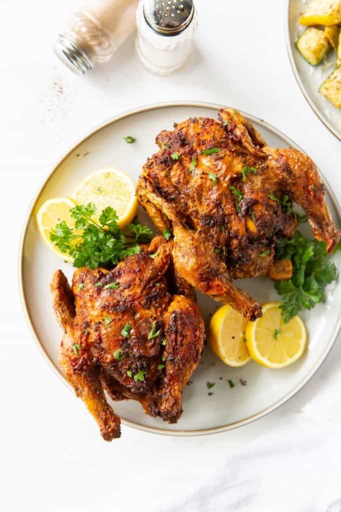 Air Fryer Cornish Hen served on a white plate with lemons and green garnish