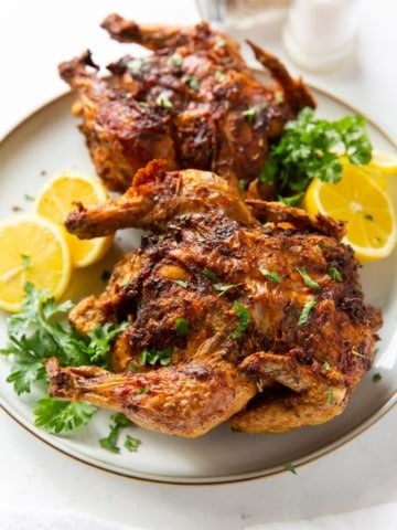 Air Fryer Cornish Hens served on a white plate with lemon halves and garnishing