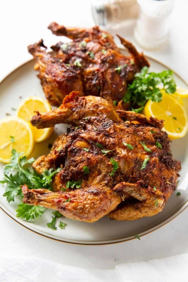 Air Fryer Cornish Hens served on a white plate with lemon halves and garnishing