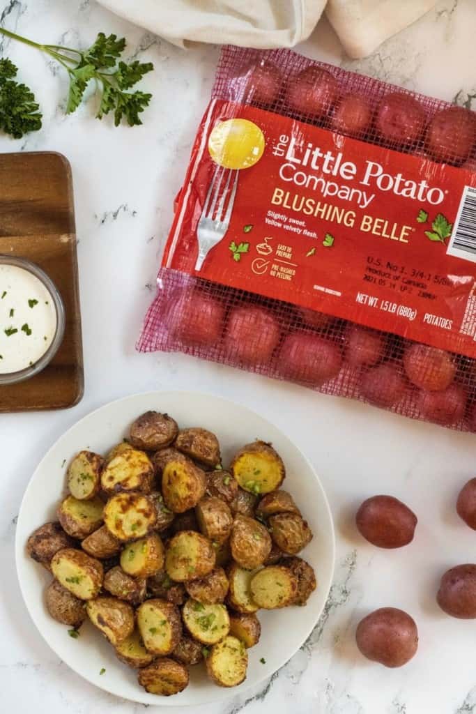 Air Fryer Ranch Potatoes on a white plate with mesh bag of Little Potato Company Blushing Belle potatoes