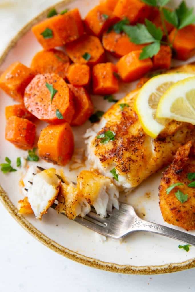 Air Fryer Tilapia with a piece flaked on a fork served with chopped cooked carrots 