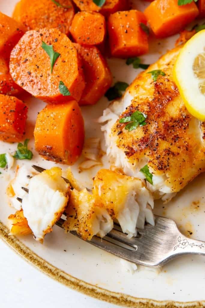 Closeup of flaked tilapia on a fork served on a white plate with carrots