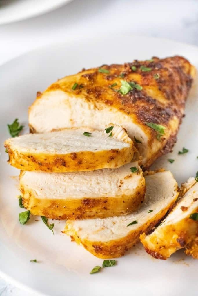 Closeup of sliced air fryer chicken breasts that were cooked from chicken on a white plate