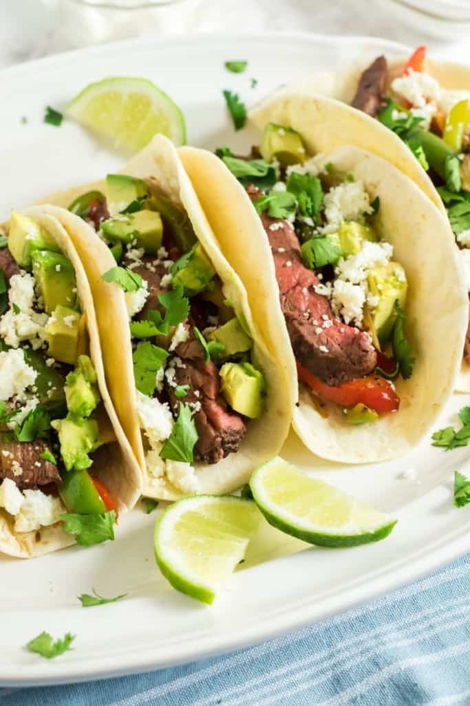 Steak Fajitas stacked next to each other on a white oval plate with lime wedges in front of them