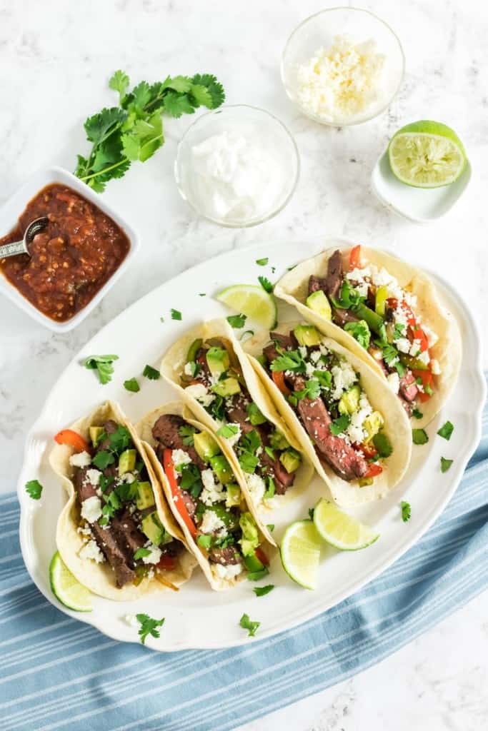 Leftover Steak Fajitas on a white oval plate surrounded by salsa, sour cream, and lime