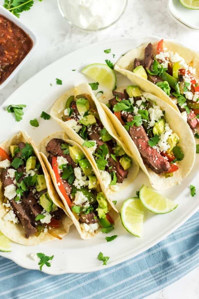 Steak fajitas on a white oval serving platter with lime wedges and cilantro around the outsides