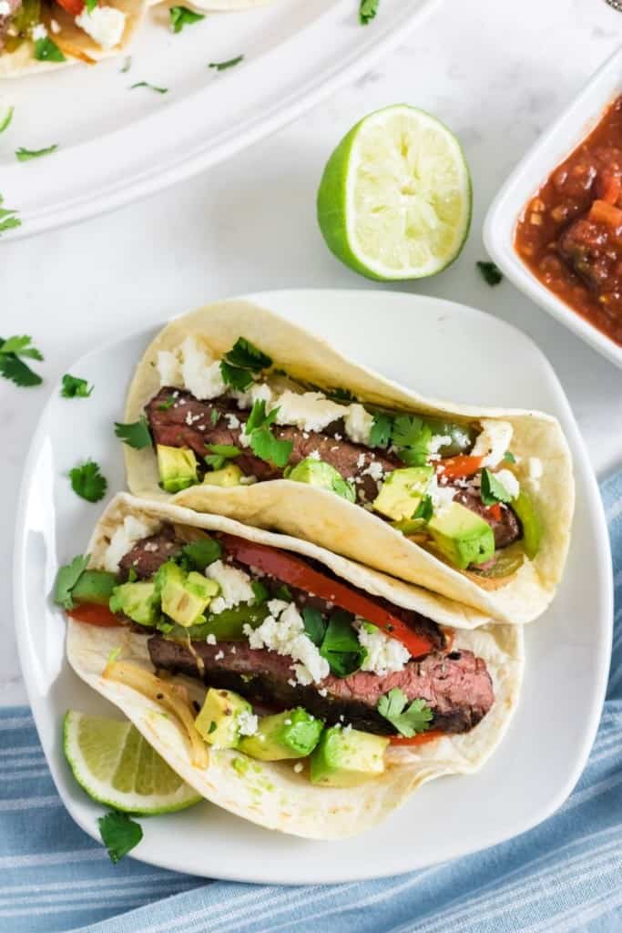 Two assembled steak fajitas on a white plate with a lime in the background