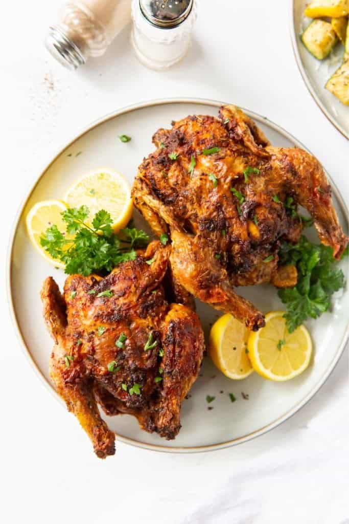 Two cooked cornish hens on a plate with lemon and parsley