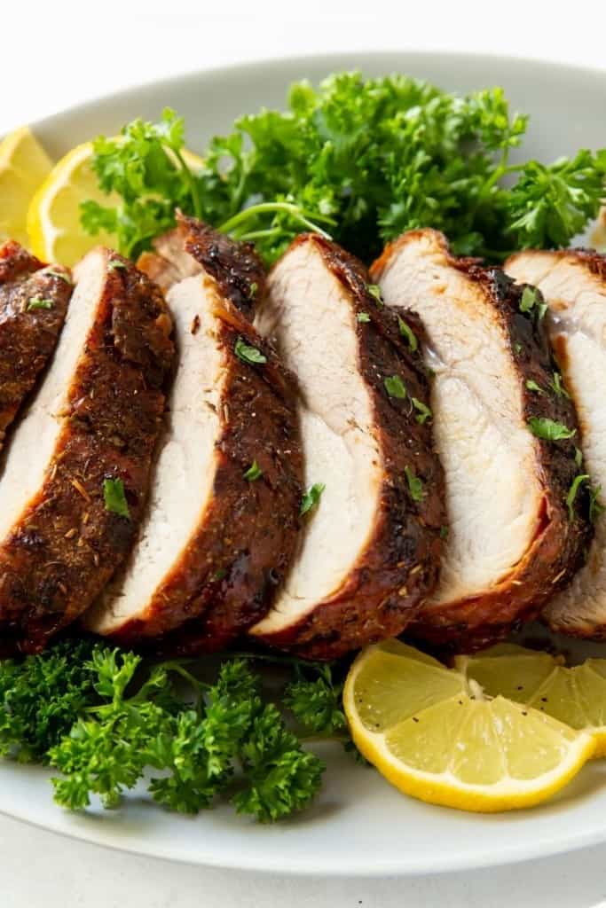 Closeup of Air Fryer Pork Loin sliced with parsley and lemons on a white plate