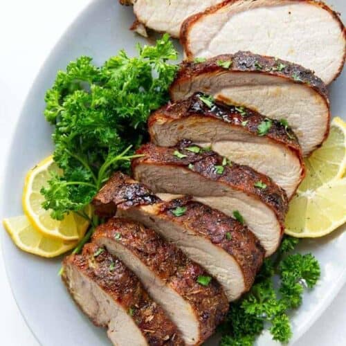 Air Fryer Pork Loin sliced on a plate with parsley and lemons