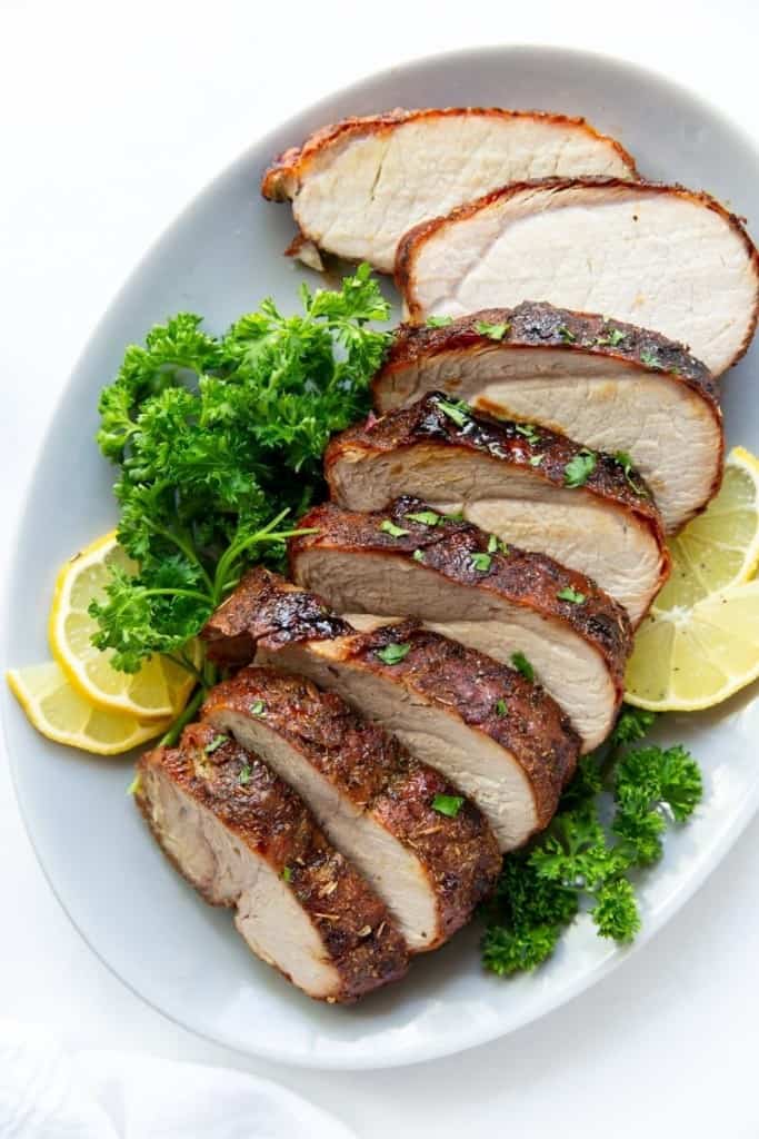 Air Fryer Pork Loin sliced on a plate with parsley and lemons