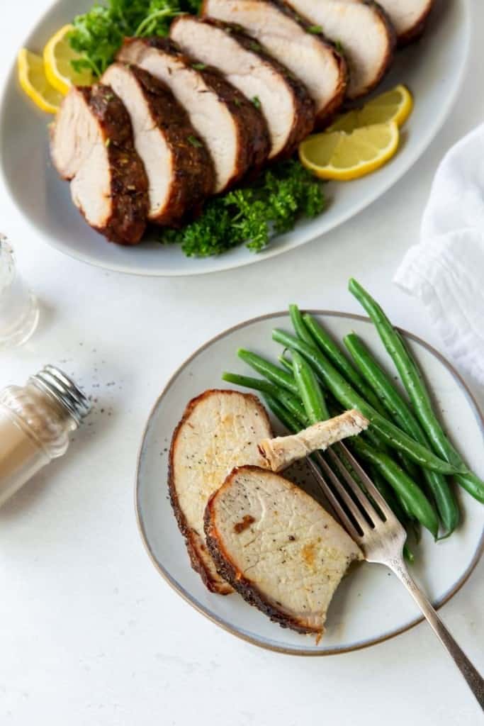 Pork loin served on a white plate with green beans with a piece cut on a fork