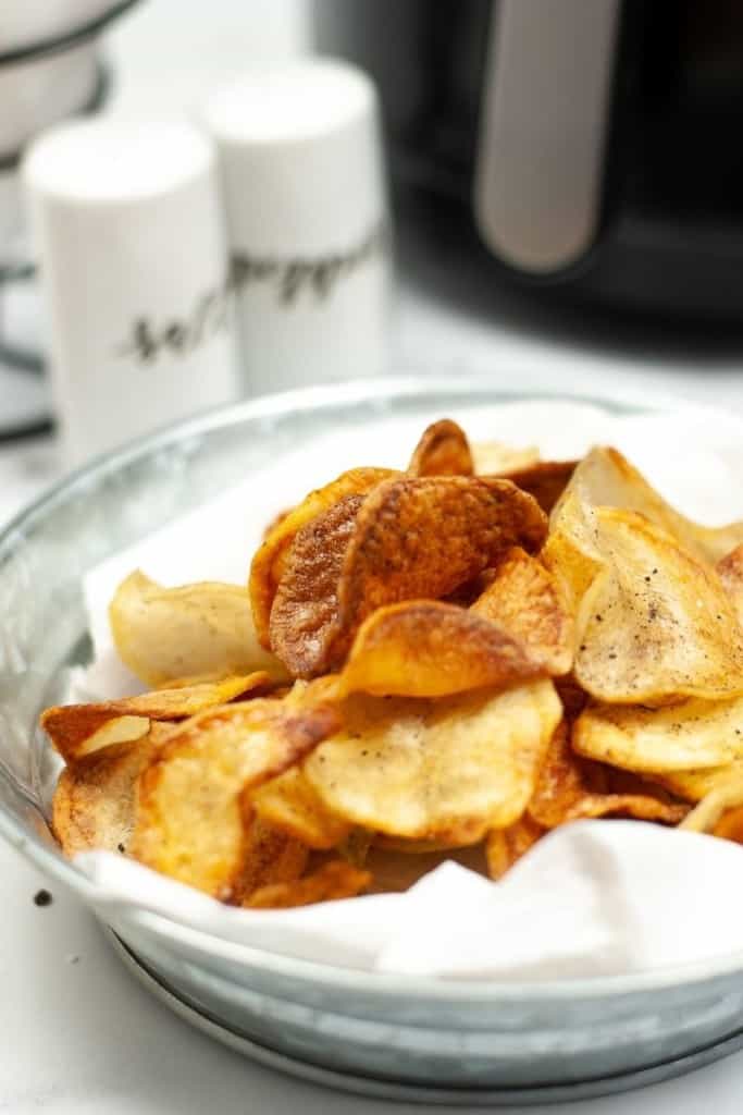 Air Fryer Potato Chips in a bowl with salt, pepper, and an air fryer in the background