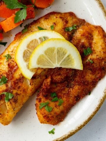 Air Fryer Tilapia on a plate with lemon wedges on top